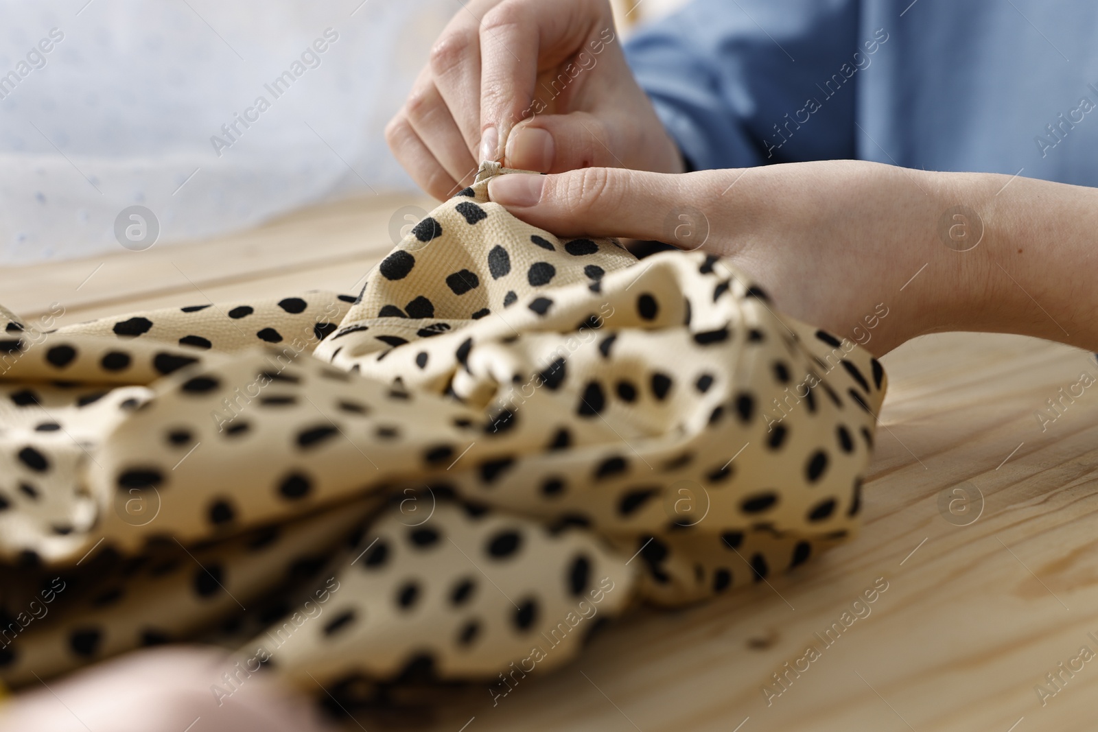 Photo of Woman sewing fabric with needle at wooden table indoors, closeup