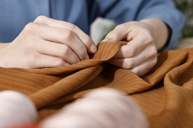 Photo of Woman sewing brown shirt with needle at table, closeup