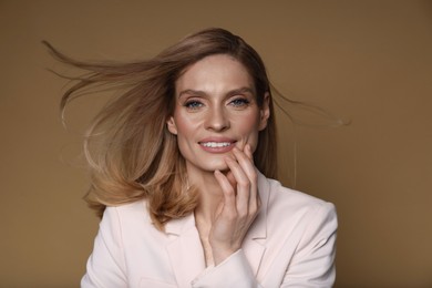 Photo of Portrait of beautiful happy woman with straight blonde hair on light brown background