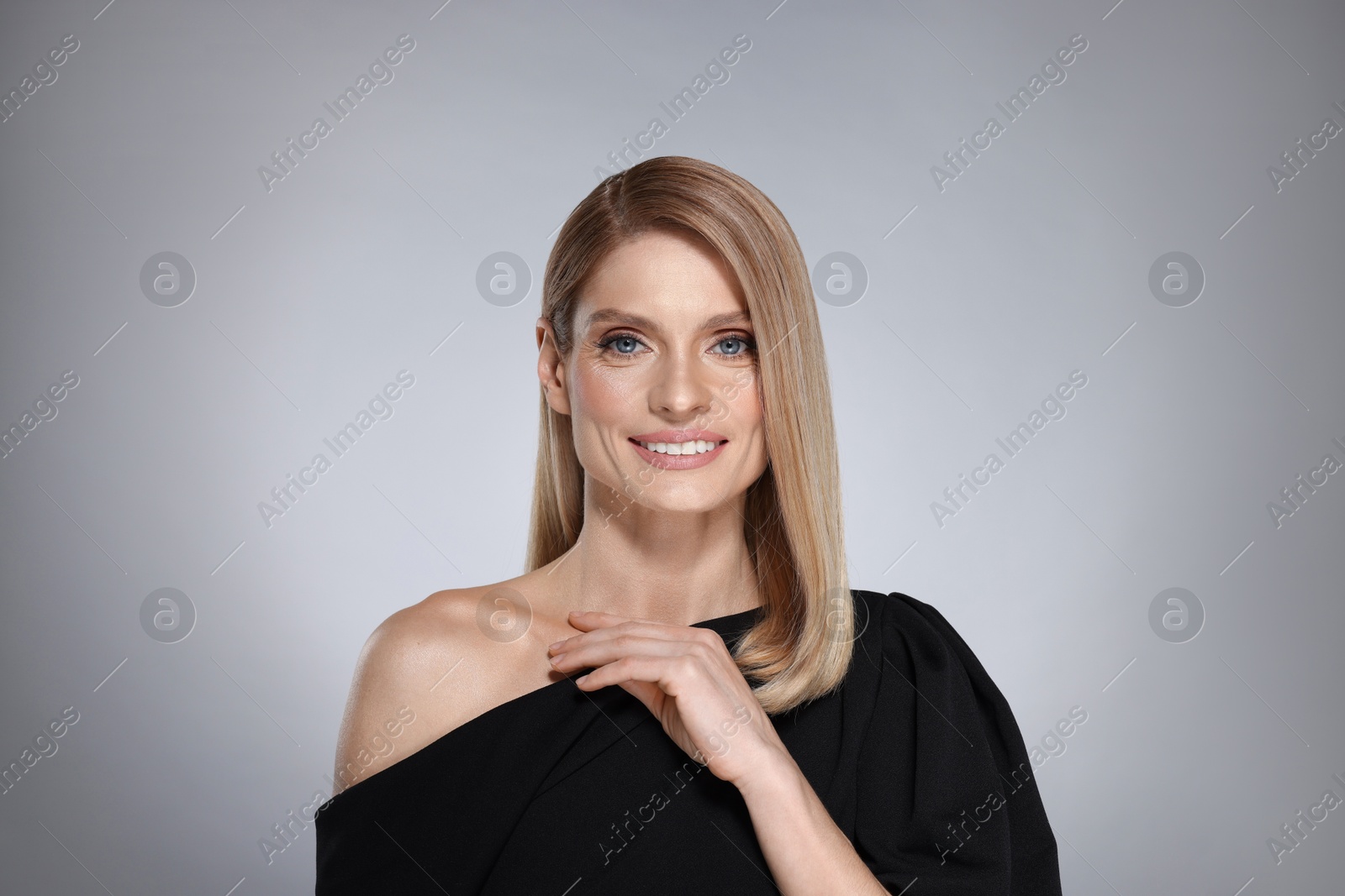 Photo of Portrait of beautiful happy woman with straight blonde hair on grey background