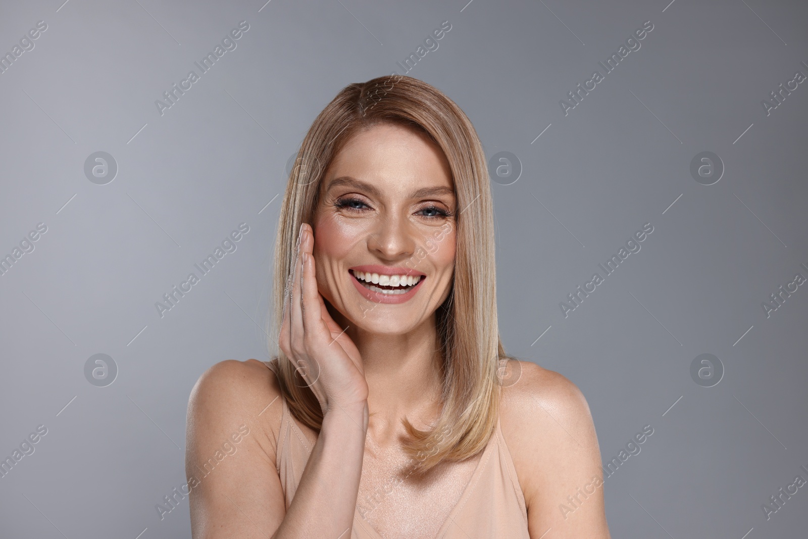 Photo of Portrait of beautiful happy woman with straight blonde hair on grey background