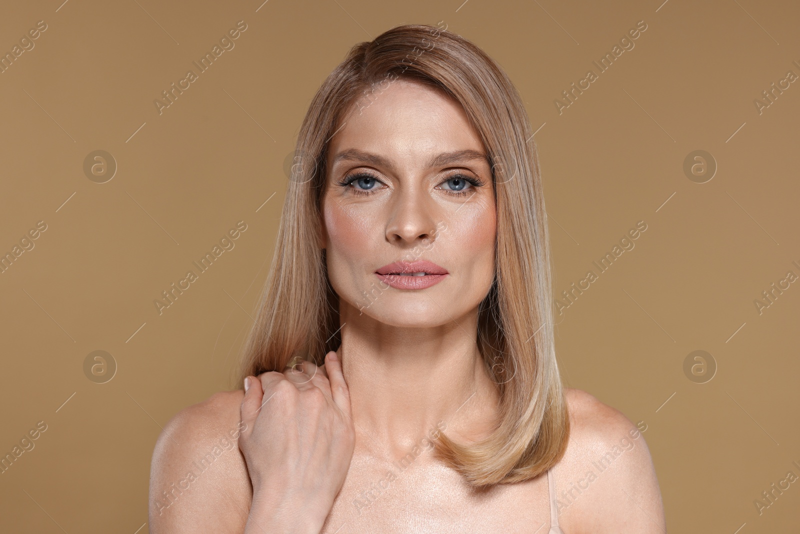 Photo of Portrait of beautiful woman with straight blonde hair on dark beige background