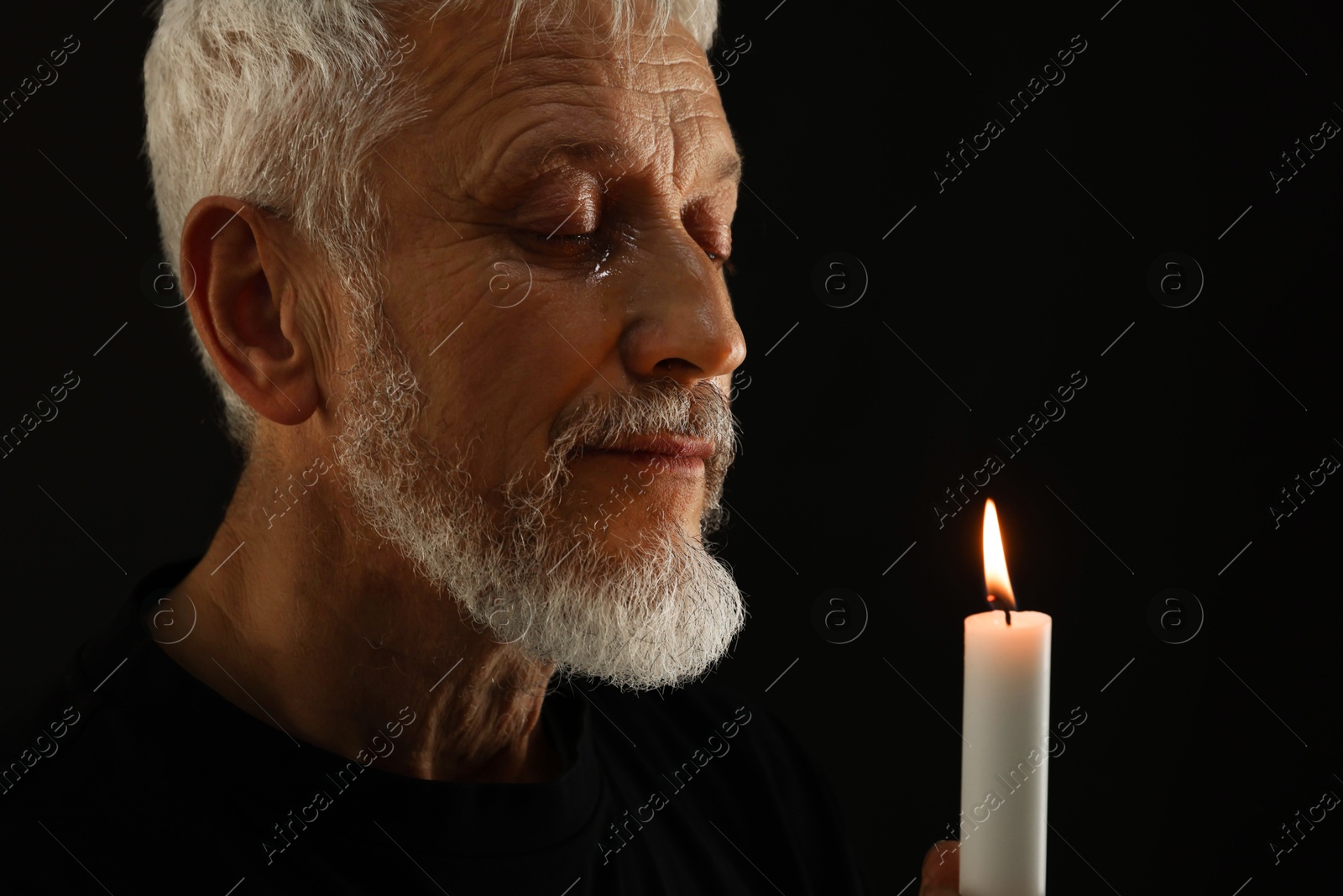 Photo of Sad senior man with burning candle crying on black background. Grieving loss