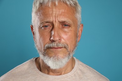 Photo of Sad senior man crying on light blue background, closeup