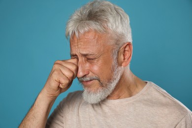 Photo of Sad senior man crying on light blue background, closeup