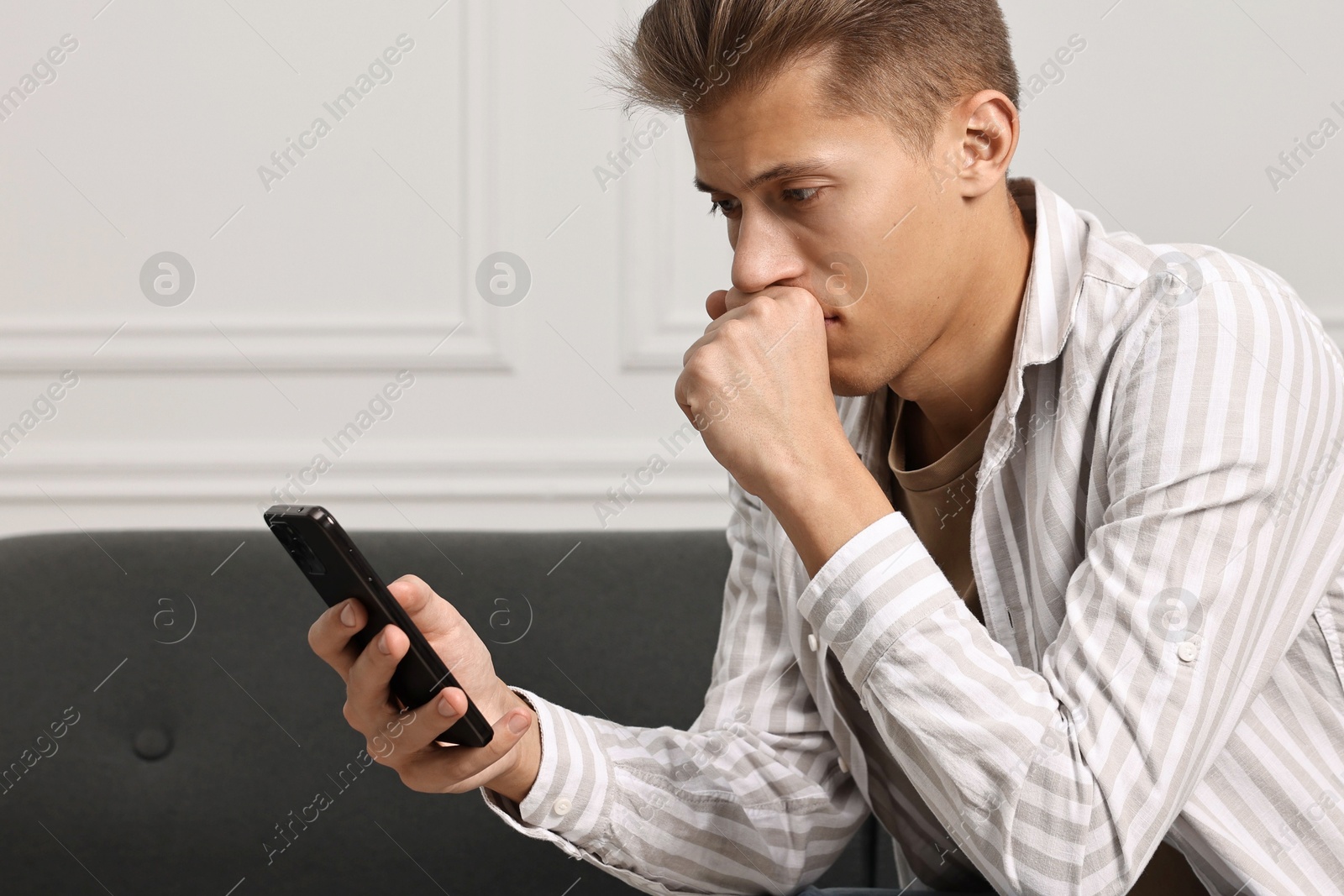 Photo of Stressed man calling hotline for mental health help on sofa at home