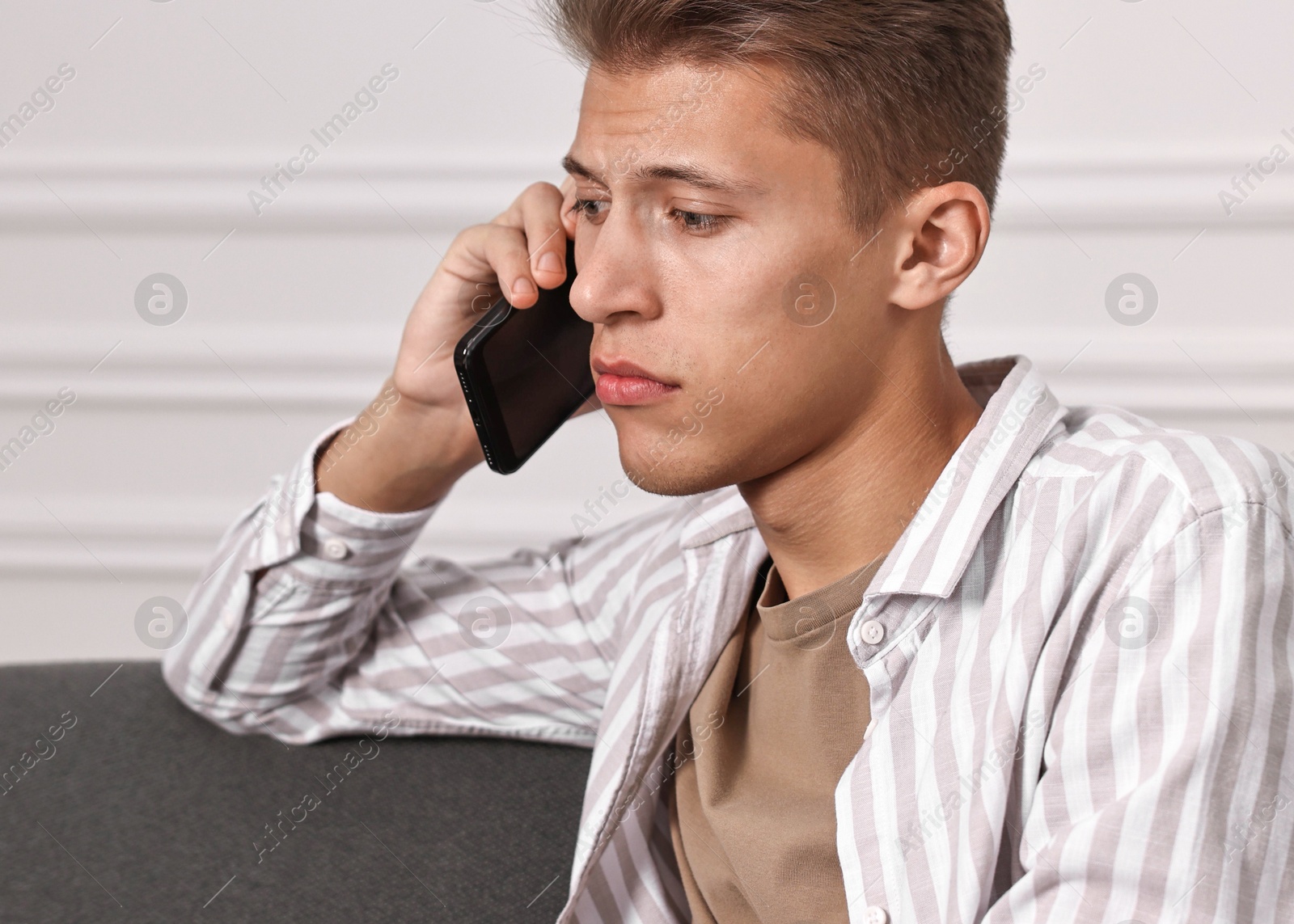 Photo of Stressed man calling hotline for mental health help on sofa at home