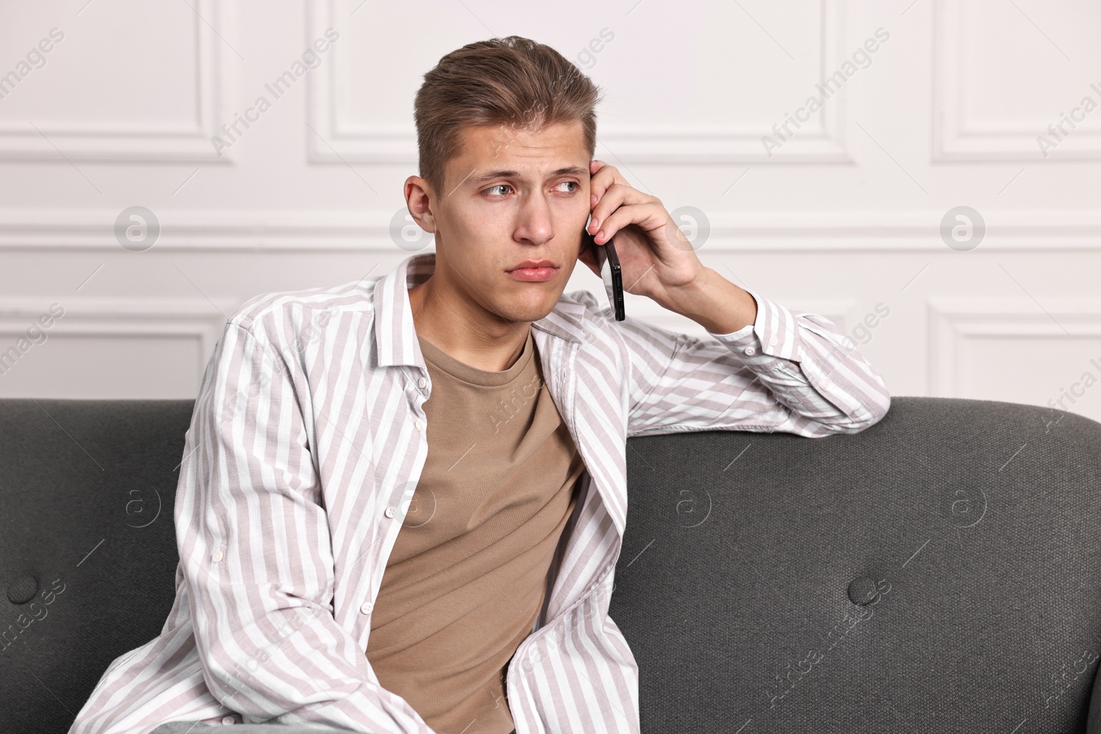 Photo of Stressed man calling hotline for mental health help on sofa at home