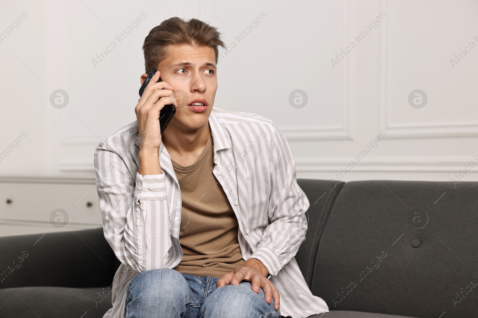 Photo of Worried man calling hotline for mental health help on sofa at home