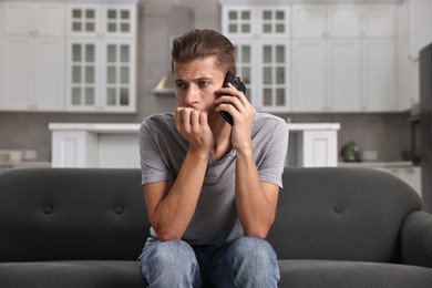 Photo of Stressed man calling hotline for mental health help on sofa in kitchen