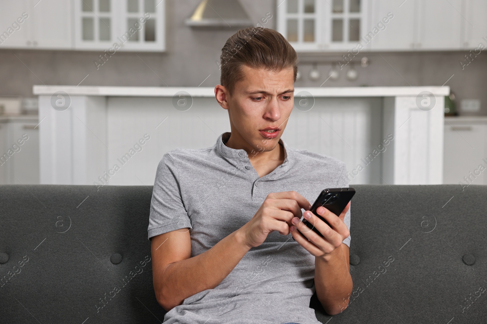 Photo of Stressed man calling hotline for mental health help on sofa in kitchen