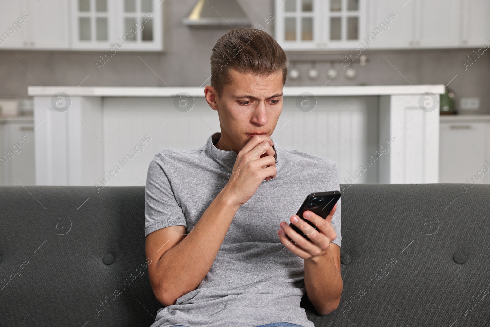 Photo of Worried man going to call hotline for mental health help on sofa in kitchen. Need for talk