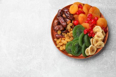 Photo of Mix of different dried fruits in bowl on light grey table, top view. Space for text