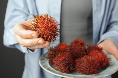 Photo of Woman holding fresh rambutans on plate against black background, closeup