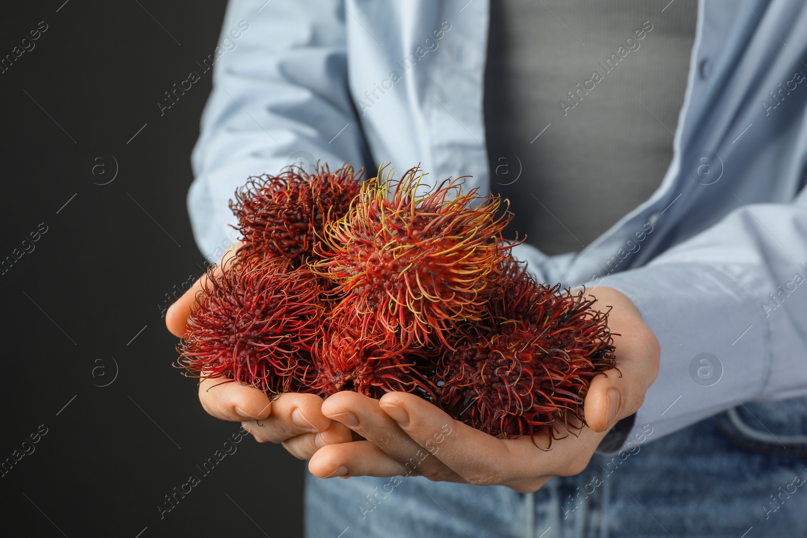 Photo of Woman holding fresh rambutans against black background, closeup