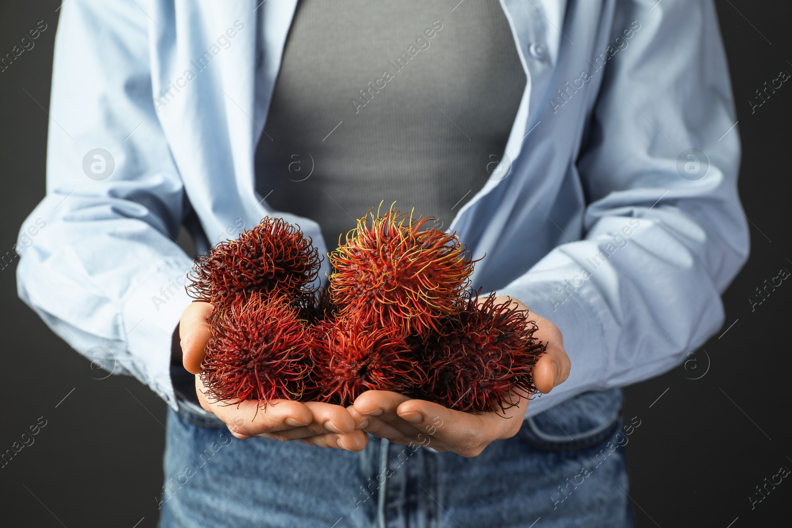 Photo of Woman holding fresh rambutans against black background, closeup