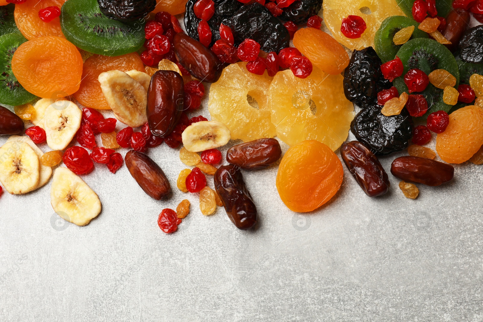 Photo of Mix of different dried fruits on gray textured table, top view. Space for text