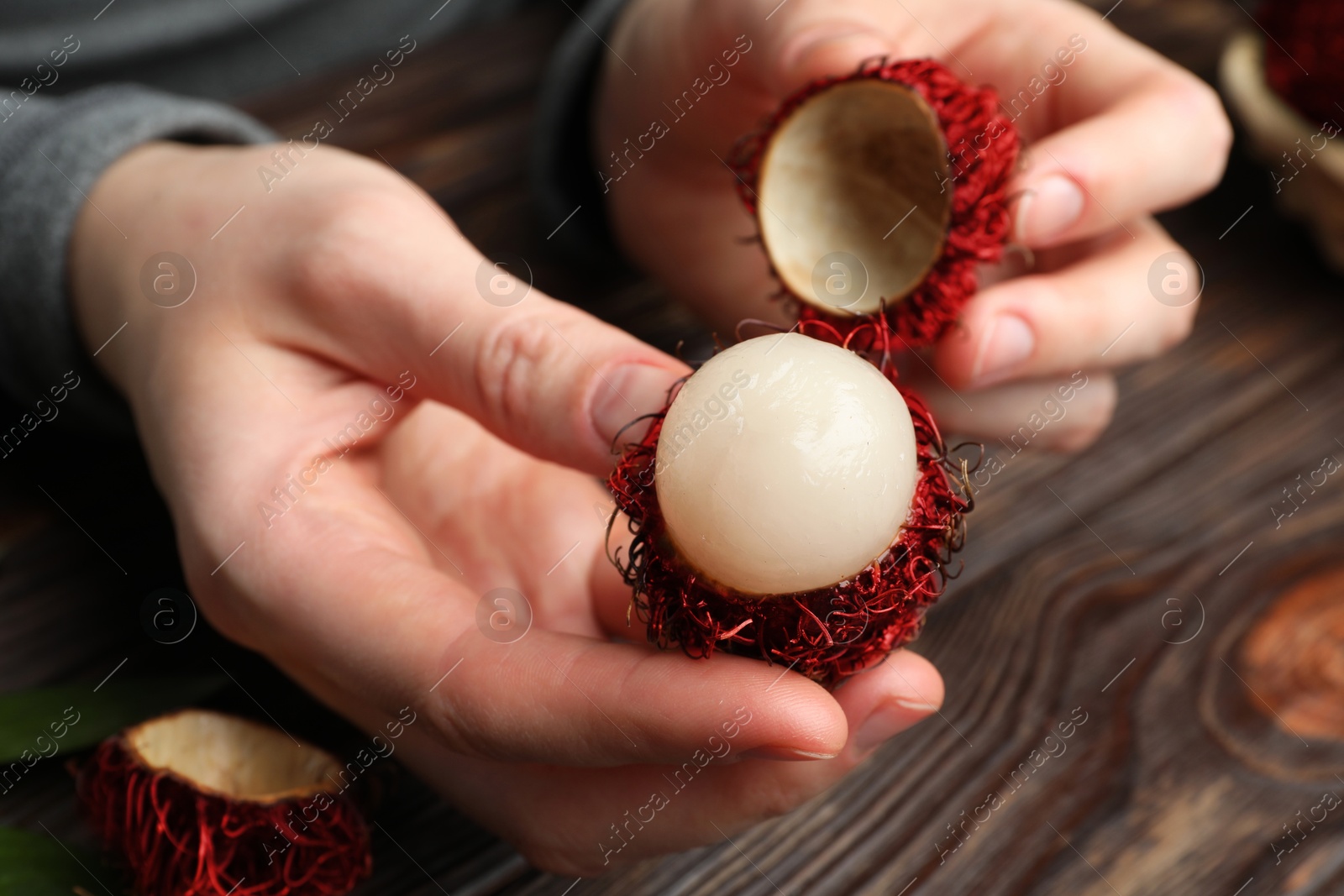 Photo of Woman peeling ripe rambutan at wooden table, closeup