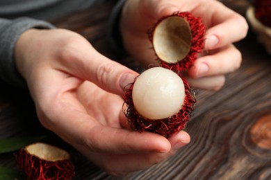 Photo of Woman peeling ripe rambutan at wooden table, closeup