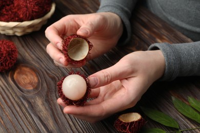 Photo of Woman peeling ripe rambutan at wooden table, closeup