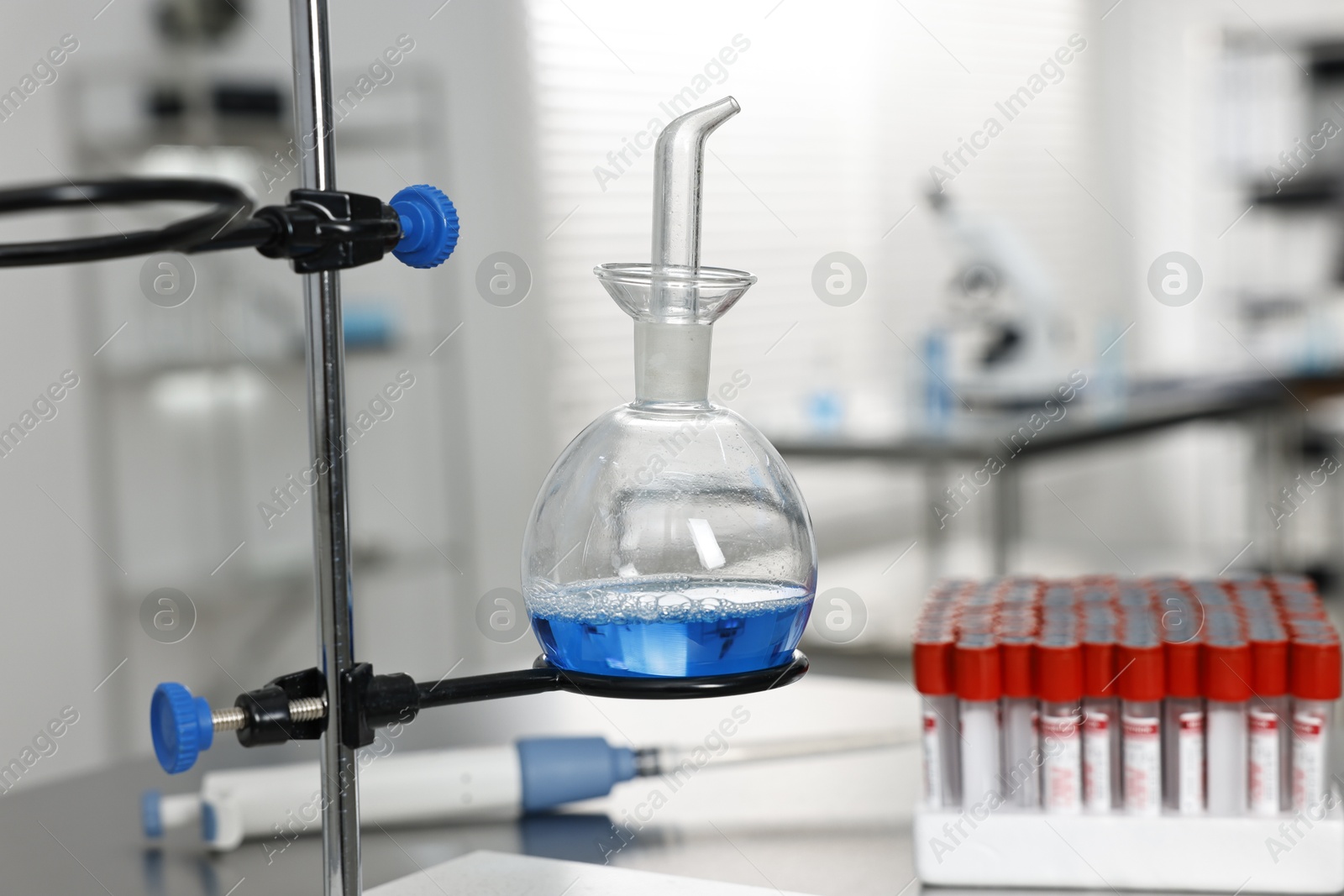 Photo of Flask with blue liquid on retort stand in laboratory, closeup