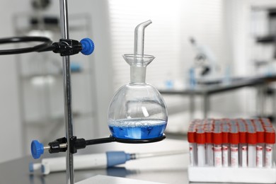 Photo of Flask with blue liquid on retort stand in laboratory, closeup