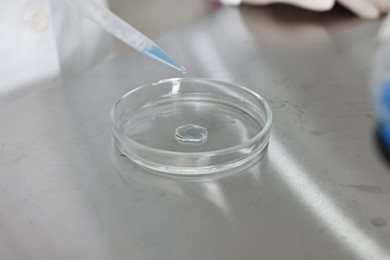 Photo of Scientist dripping reagent into Petri dish at table in laboratory, closeup