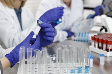 Photo of Scientist with vial and test tubes working in laboratory, closeup