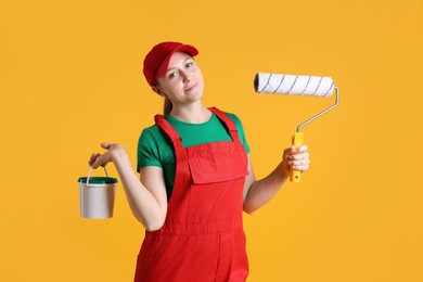 Photo of Professional painter with roller and bucket of paint on orange background