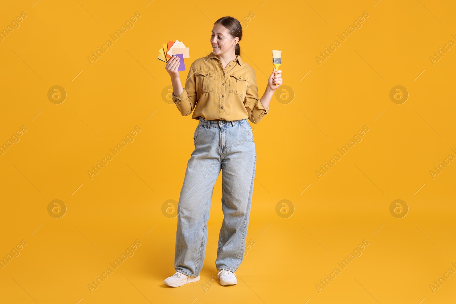 Photo of Woman with paintbrush and color samples on orange background