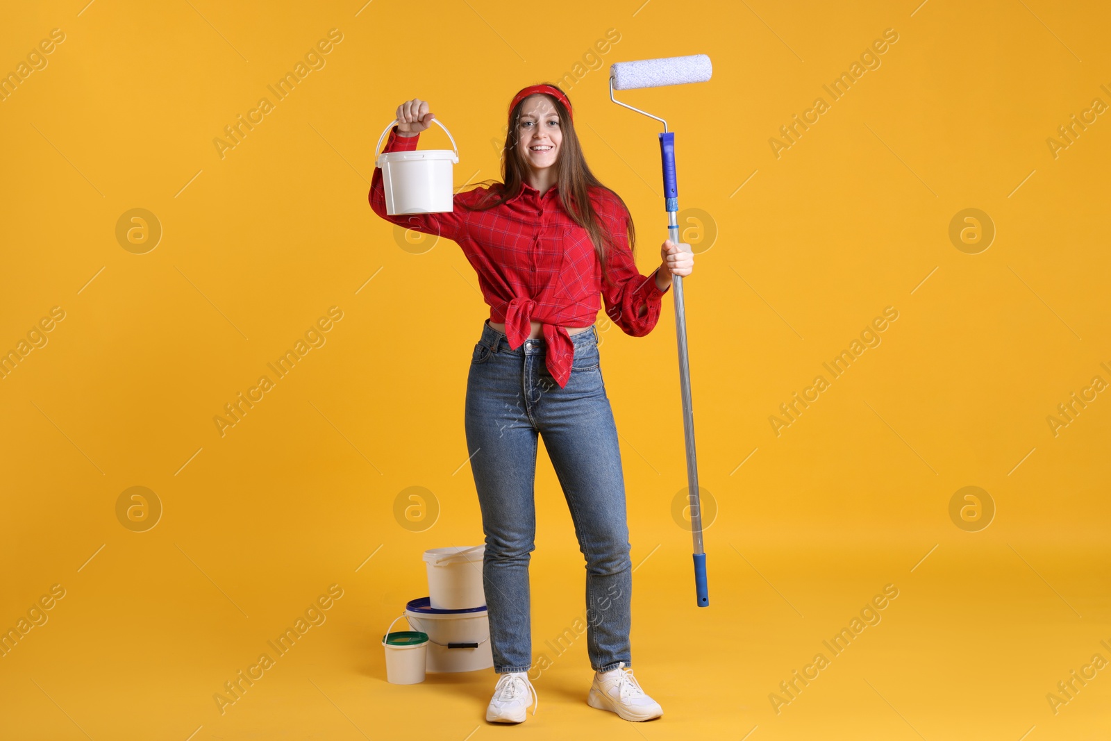 Photo of Woman with roller and buckets of paint on orange background