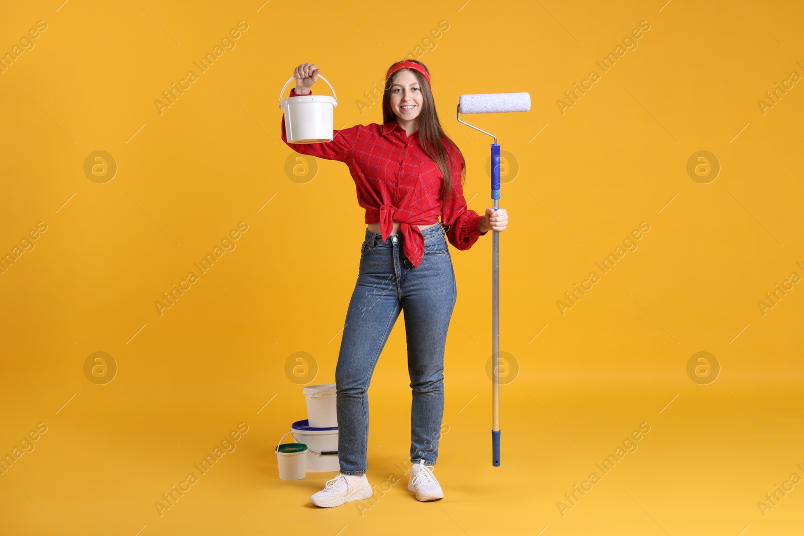 Photo of Woman with roller and buckets of paint on orange background