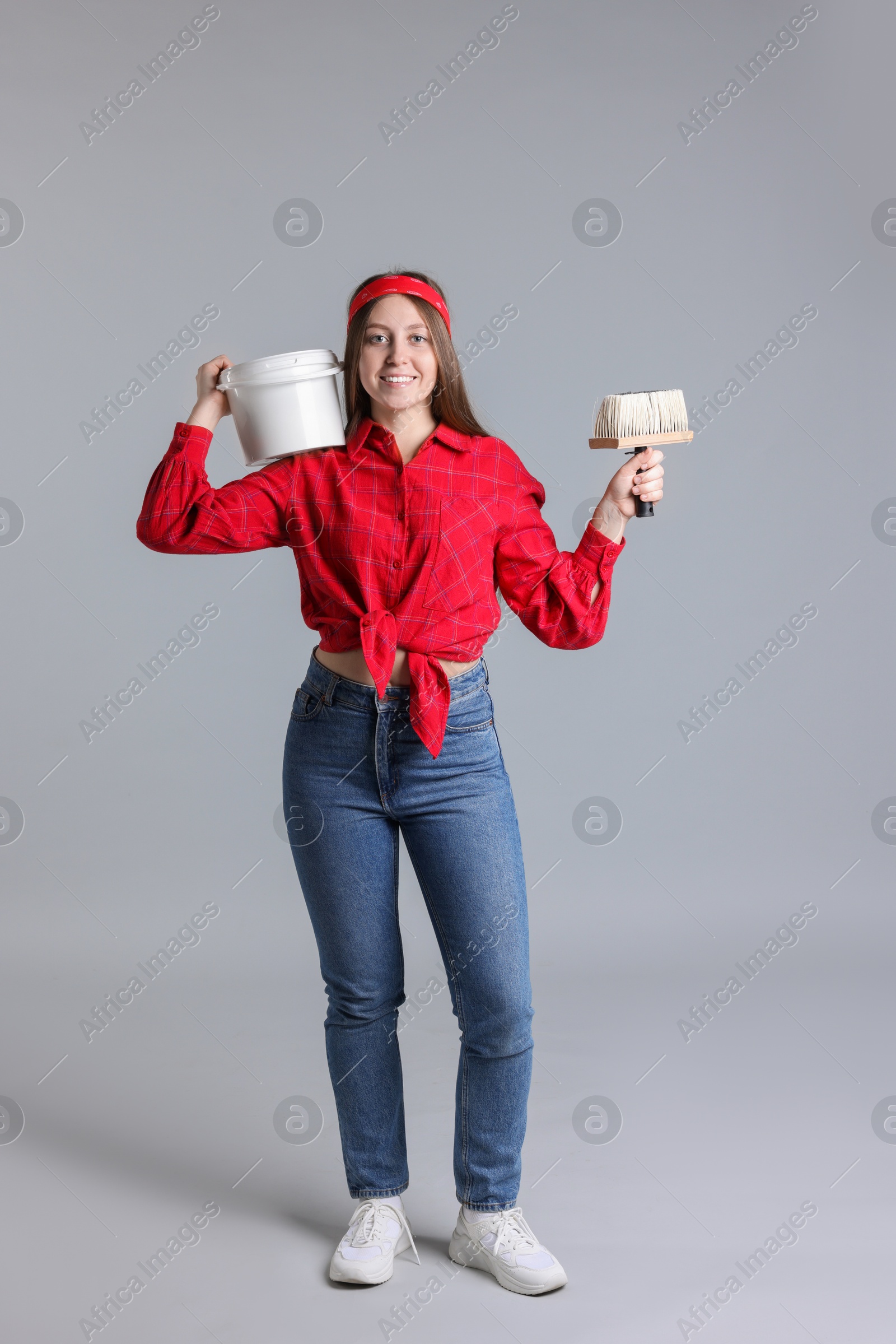 Photo of Woman with brush and bucket of paint on light grey background