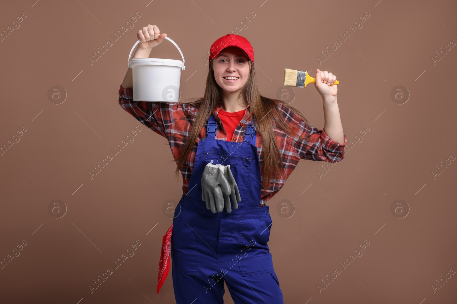 Photo of Professional painter with brush and bucket of paint on brown background