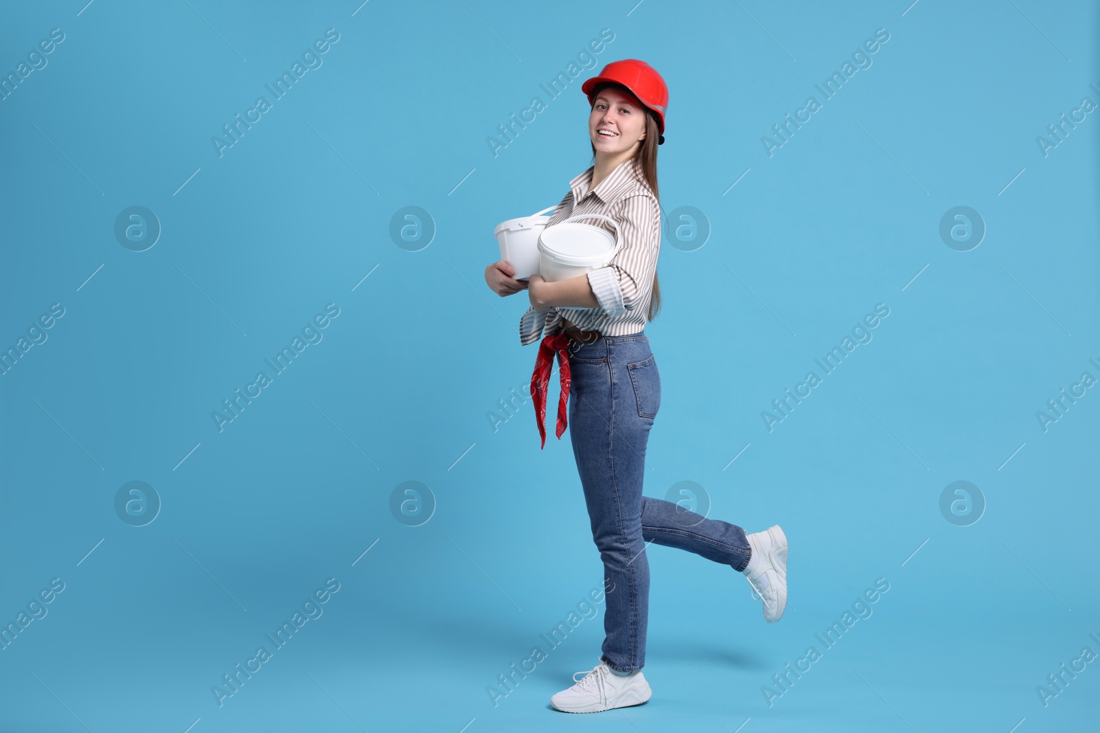 Photo of Woman wearing hardhat with buckets of paint on light blue background