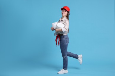 Photo of Woman wearing hardhat with buckets of paint on light blue background