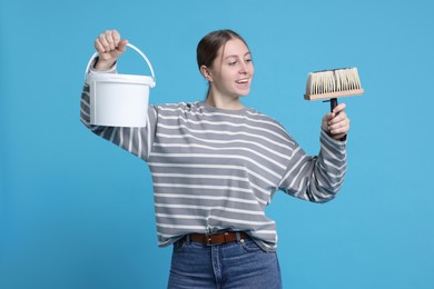 Photo of Woman with brush and bucket of paint on light blue background