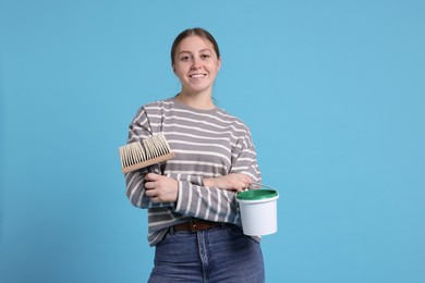 Photo of Woman with brush and bucket of paint on light blue background