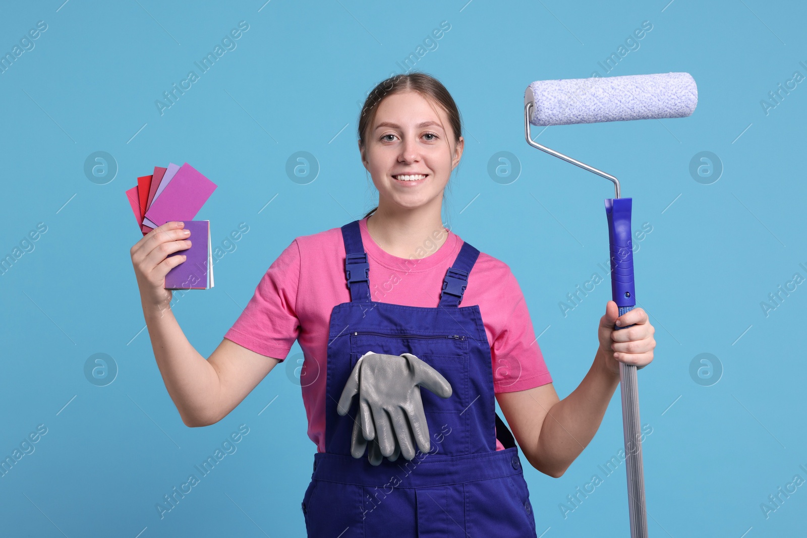 Photo of Professional painter with roller and color samples on light blue background