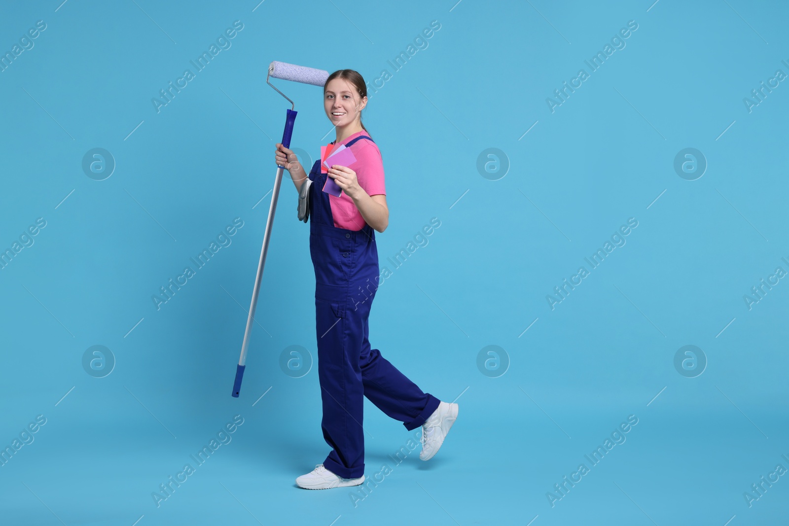 Photo of Professional painter with roller and color samples on light blue background