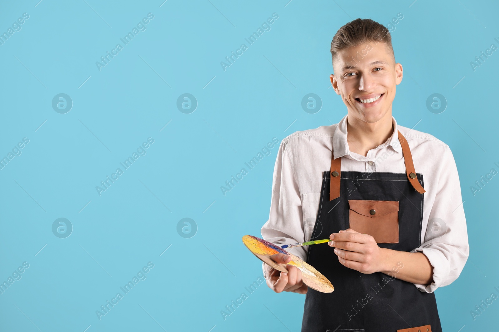 Photo of Smiling man with palette and paintbrush on light blue background. Space for text