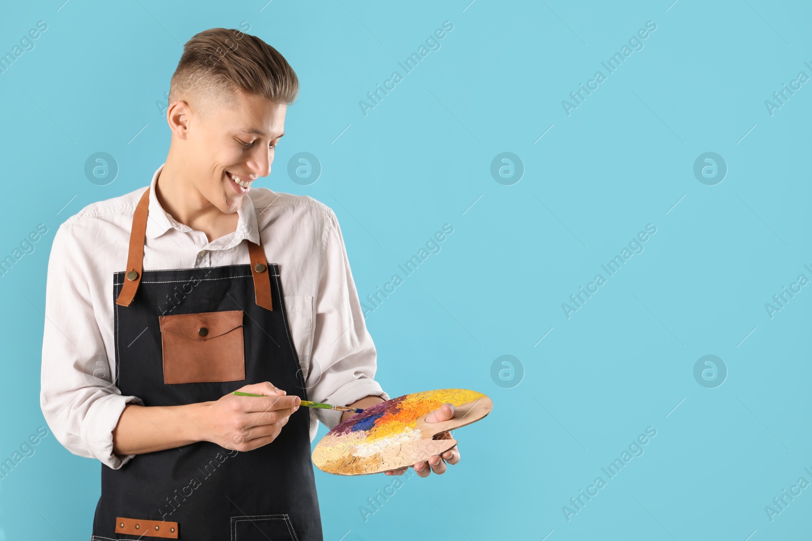 Photo of Smiling man with palette and paintbrush on light blue background. Space for text