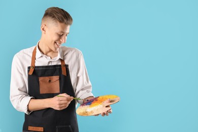 Photo of Smiling man with palette and paintbrush on light blue background. Space for text