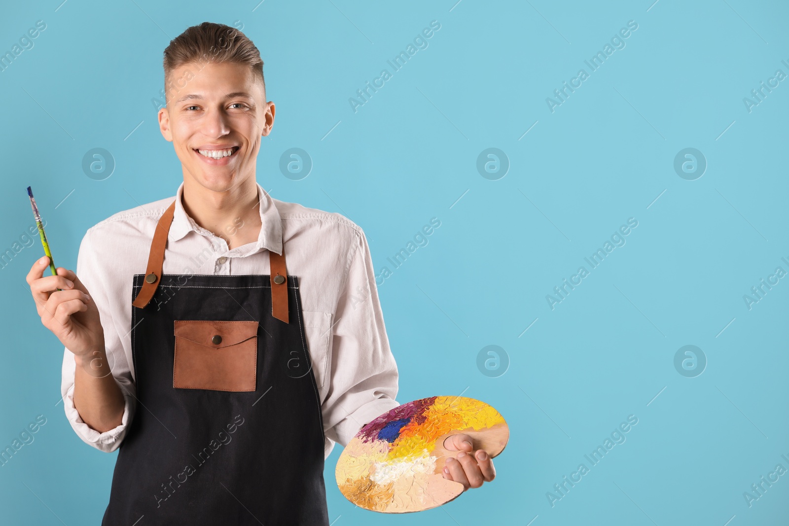 Photo of Smiling man with palette and paintbrush on light blue background. Space for text