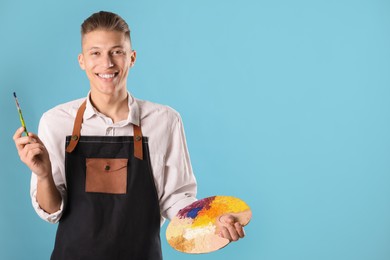 Photo of Smiling man with palette and paintbrush on light blue background. Space for text