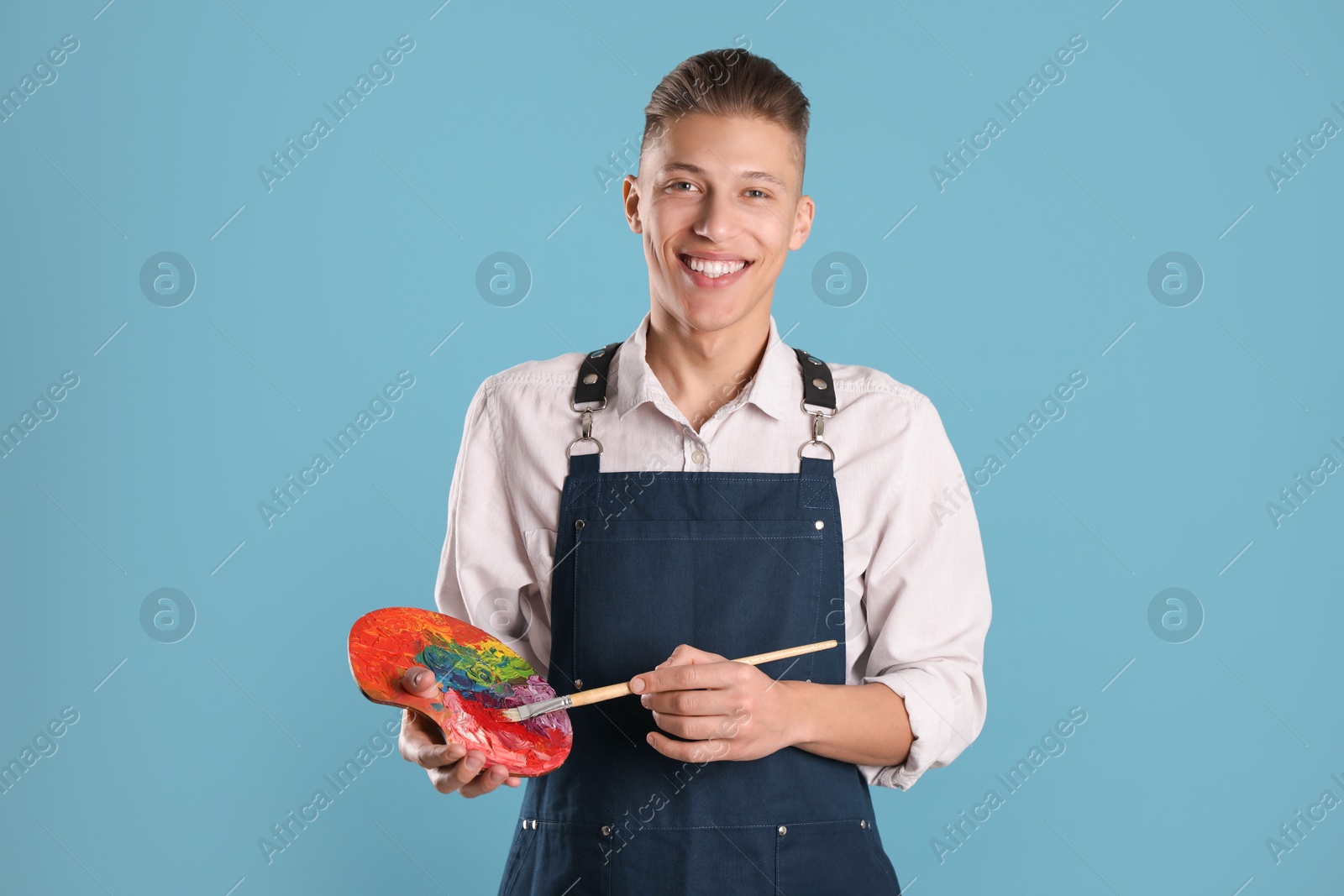 Photo of Smiling man with palette and paintbrush on light blue background