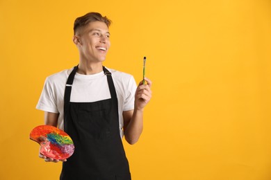 Photo of Smiling man with palette and paintbrush on orange background. Space for text