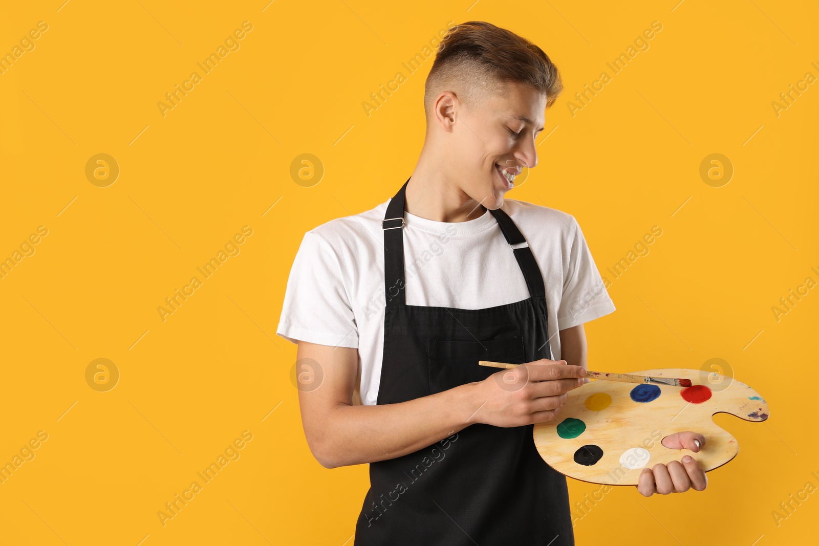 Photo of Smiling man with wooden palette and paintbrush on orange background. Space for text