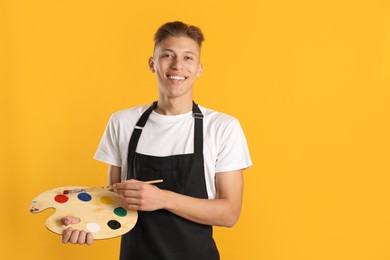 Photo of Smiling man with wooden palette and paintbrush on orange background. Space for text