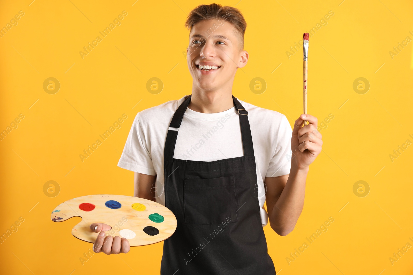 Photo of Smiling man with wooden palette and paintbrush on orange background